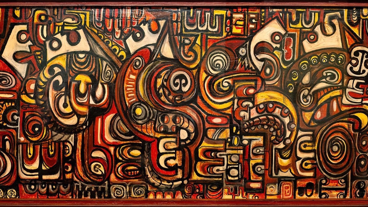 The image is a photograph of an art piece by Fred Graham. There are a lot of curves and traditional Māori patterns in the piece, with a warm colour pallet full of browns, yellows, and oranges. Visible are multiple koru, swirls, and circles.