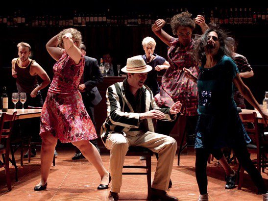 A lively event on stage with brass band musicians and dancing singers